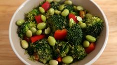 a white bowl filled with broccoli, tomatoes and green beans on top of a wooden table