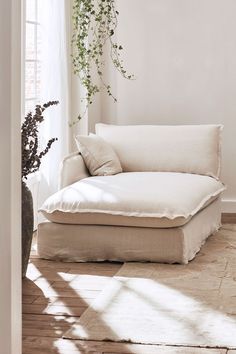 a white couch sitting in front of a window next to a vase filled with flowers