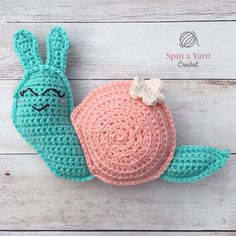 a crocheted snail laying on top of a white wooden floor next to a ball of yarn