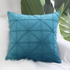 a blue pillow sitting on top of a white bed next to a green leafy plant