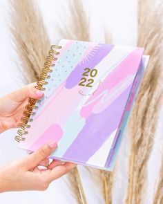 a hand holding a planner with the number twenty two on it, in front of some dry grass