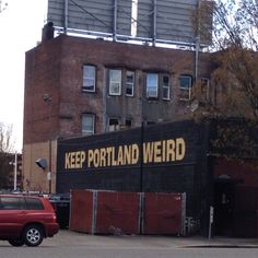 a red car is parked in front of a building with a sign that reads keep portland weird