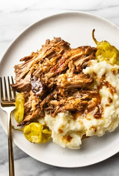 a white plate topped with mashed potatoes covered in meat and peppers next to a fork