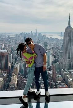 a man and woman standing on top of a building in new york city with the empire building in the background