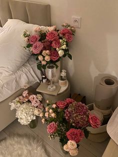 flowers are arranged in vases on a nightstand next to a bed with white sheets