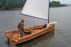 a man standing on the front end of a small wooden boat in water with a sail