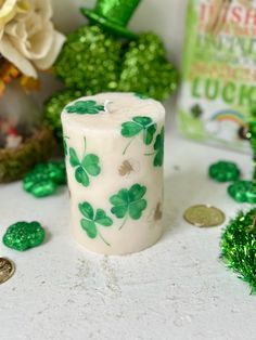 a white candle with green shamrocks on it next to some coins and other decorations