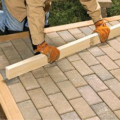 two men are working on some wooden planks in front of a building with brick pavers