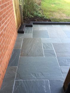 a black slate patio with brick wall and grass in the back ground, next to a red brick building