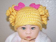 a baby wearing a yellow knitted hat with pink bows on it's head