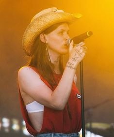 a woman wearing a cowboy hat and holding a microphone in her hand while standing on stage