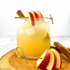 an apple cider is garnished with cinnamon sticks and sliced apples on a wooden board