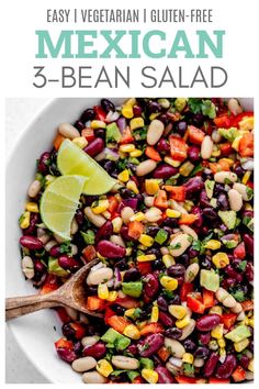 mexican bean salad in a white bowl with a wooden spoon and lime on the side