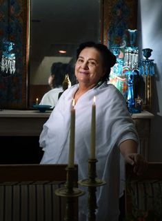 a woman standing next to two candles in front of a mirror