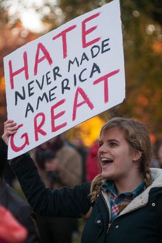 a woman holding a sign that says hate never made america great