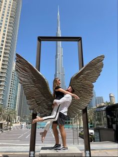 a man and woman standing in front of an angel statue with the burj building in the background