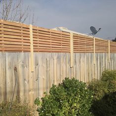 a wooden fence with a satellite dish mounted on it's top, next to shrubbery