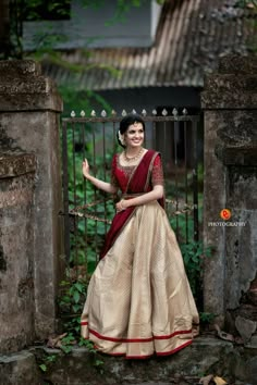 a woman in a red and beige dress standing by a gate