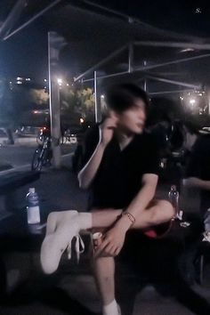 two people sitting on the ground talking on their cell phones and drinking wine at night