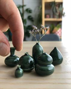 a hand is touching some tiny green vases