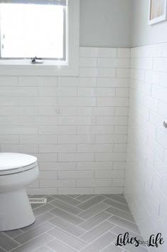 a white toilet sitting inside of a bathroom next to a window on top of a tiled floor