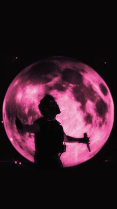 a person standing in front of a pink moon