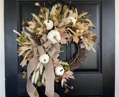 a wreath with white pumpkins, leaves and pine cones is hanging on the front door