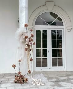 a tall white pole with flowers on it next to a building and two doors that are open