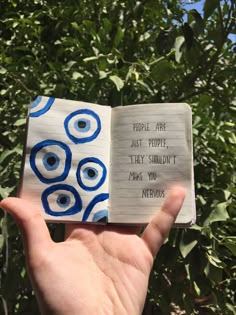 a hand holding an open book with words on it and blue circles painted on the pages