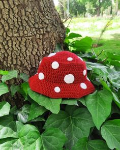 a crocheted red hat with white polka dots on it sitting next to a tree