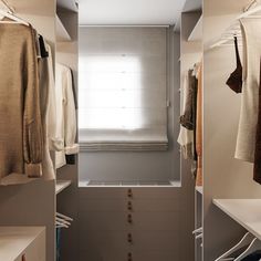 an open closet with clothes hanging on the shelves and in front of it is a window