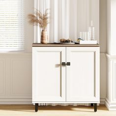 a white cabinet sitting in front of a window next to a vase with flowers on it