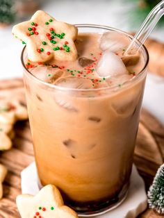 a glass filled with iced coffee and decorated cookies on top of a wooden tray next to christmas decorations