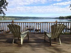 two lawn chairs sitting on top of a wooden deck next to a body of water