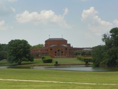 a large red brick building sitting on top of a lush green field next to a lake