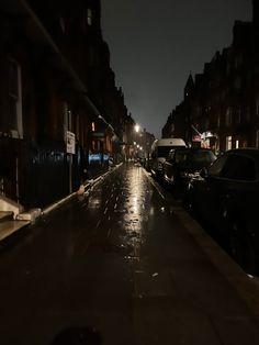 a wet street at night with cars parked on the side