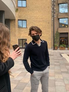 a man wearing a face mask while standing next to a woman holding a cell phone