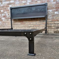 a black metal bed frame sitting in front of a brick wall with a flat screen tv mounted to it's side