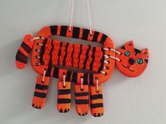 an orange and black animal made out of toothpicks on a white wall with string