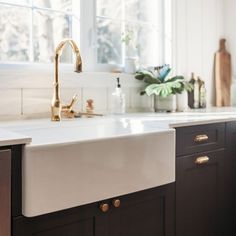 a white kitchen sink sitting under a window next to a wooden counter top with brass faucets