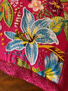 a pink pillow with blue and yellow flowers on it sitting on a wooden floor next to a red doily