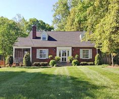 a red brick house sitting in the middle of a lush green field next to trees