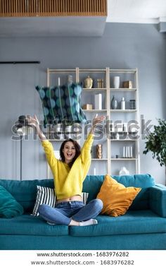 a woman is sitting on the couch with her arms in the air and smiling at the camera