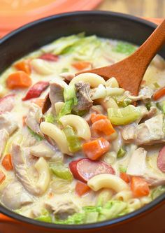 a wooden spoon is in a bowl filled with pasta and meat soup on an orange plate