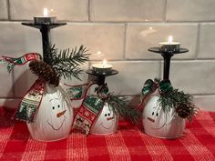 three candles are decorated with snowmen and pine cones on a red checkered tablecloth