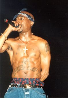 a shirtless man holding a microphone in his right hand and wearing blue jeans on the other side