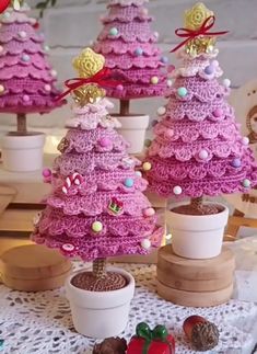 crocheted christmas trees are displayed in small pots on a doily covered table