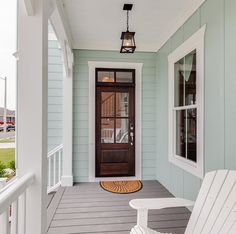 a white chair sitting on top of a porch next to a wooden door and window