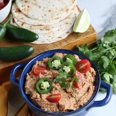 a blue bowl filled with hummus and vegetables next to tortilla chips on a cutting board