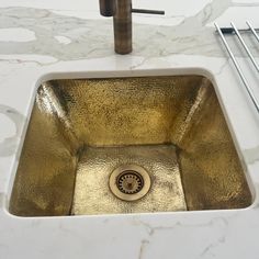 a gold sink in the middle of a marble counter top with stainless steel utensils